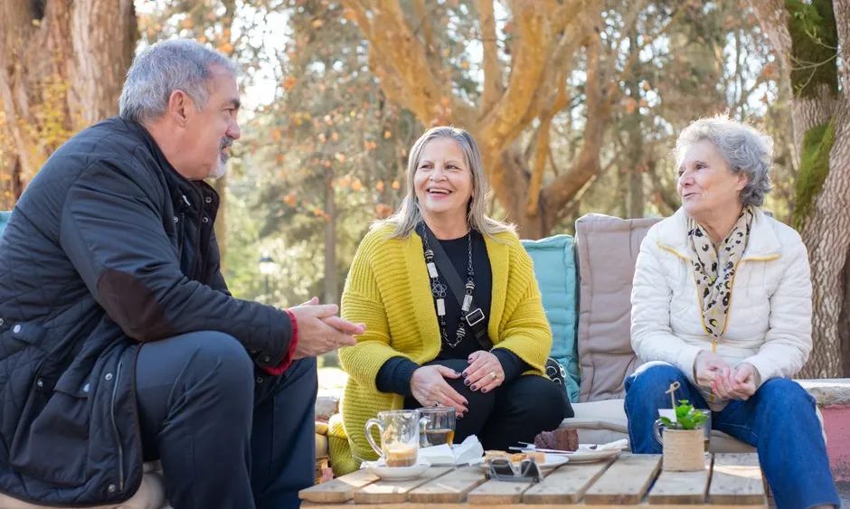 Three seniors laughing together outdoors over tea