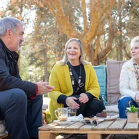 Three seniors laughing together outdoors over tea