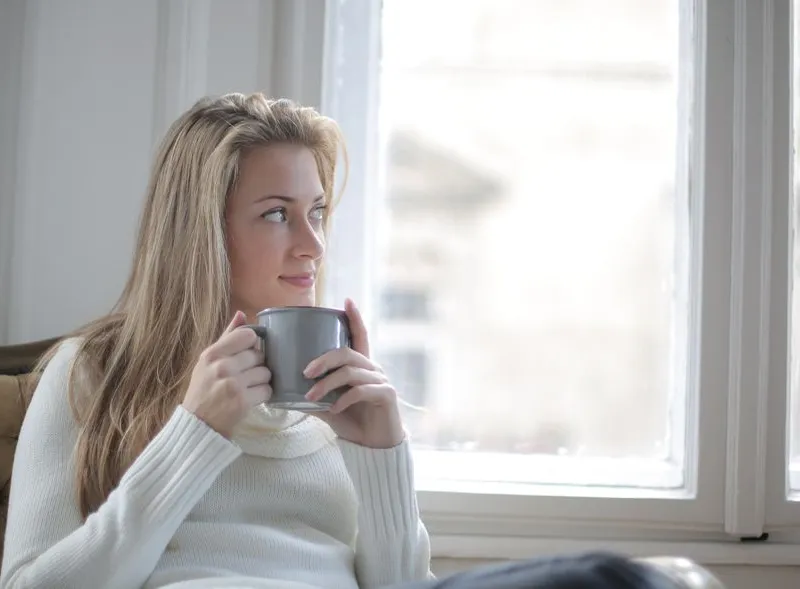 A woman relaxing with a cup of tea by a window